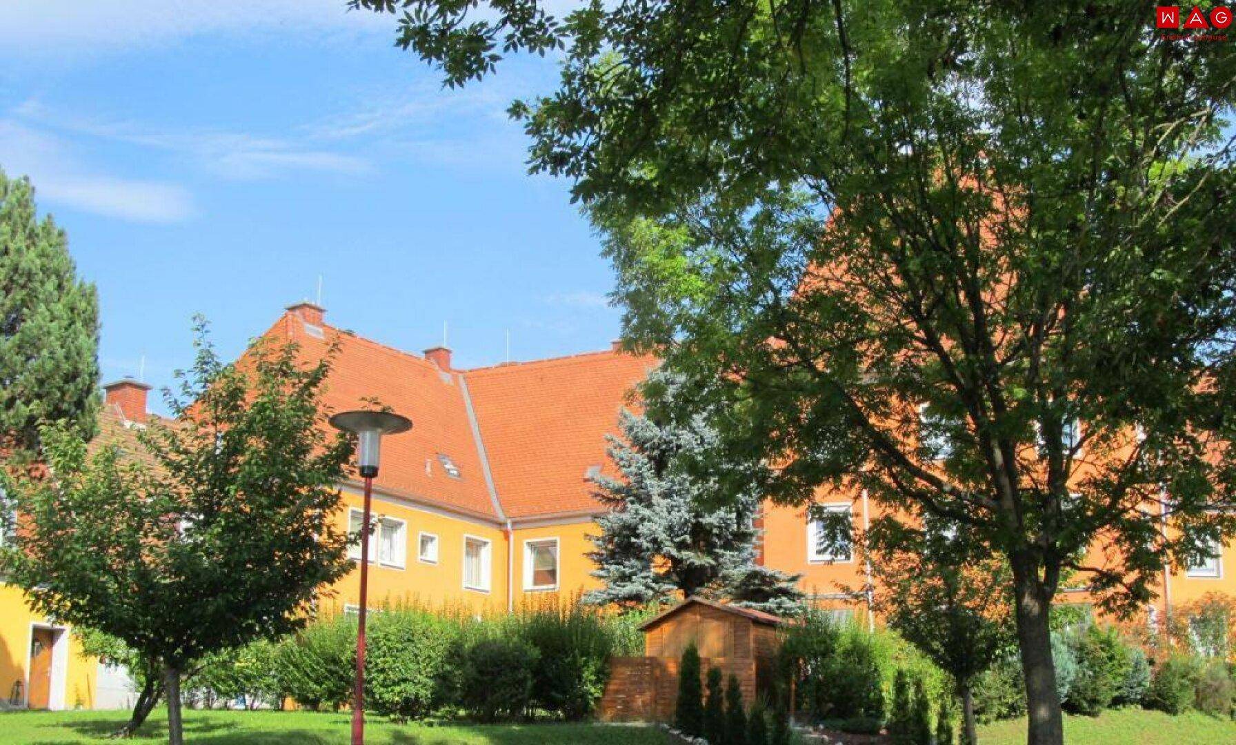 Wohngebäude mit orangerotem Dach, umgeben von Bäumen und gepflegten Grünflächen.