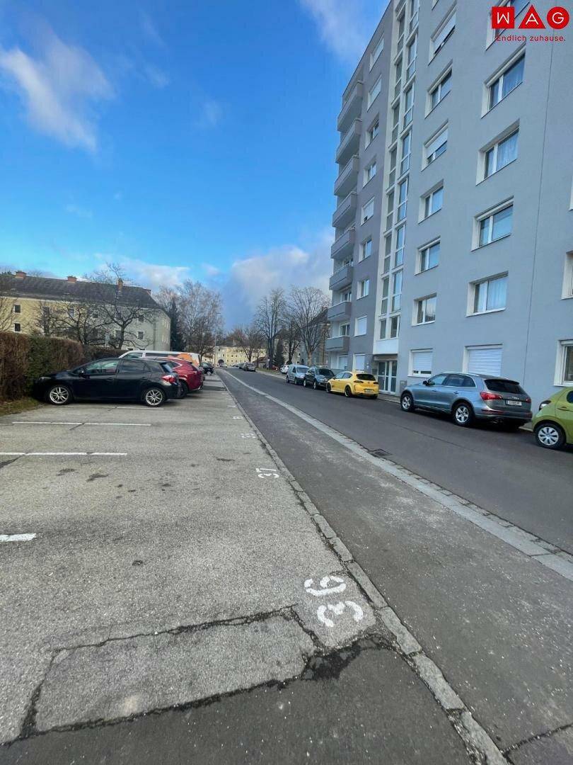 Blick auf eine Wohnstraße mit parkenden Fahrzeugen und dem modernen Mehrfamilienhaus im Hintergrund.