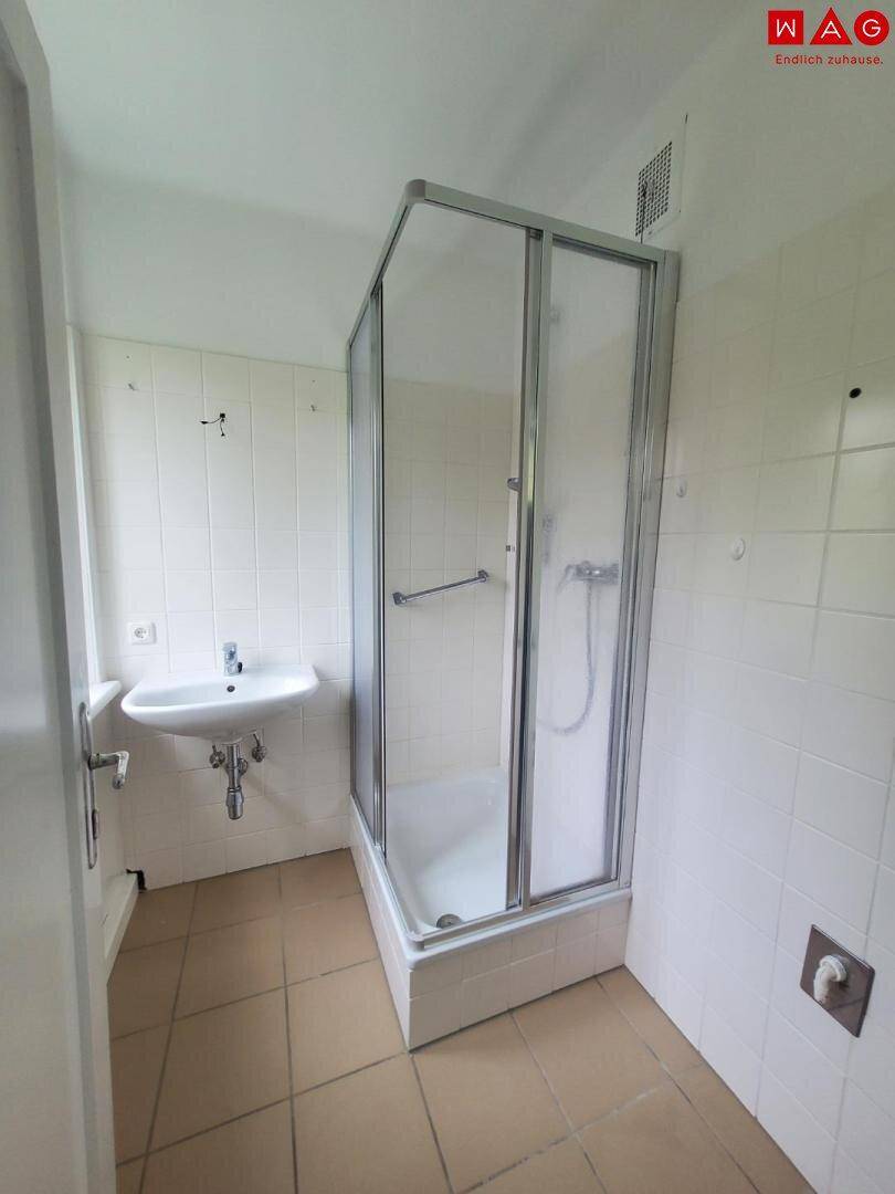 Funktionales Badezimmer mit Duschkabine, Waschbecken und hellen Fliesen an Wänden und Boden.