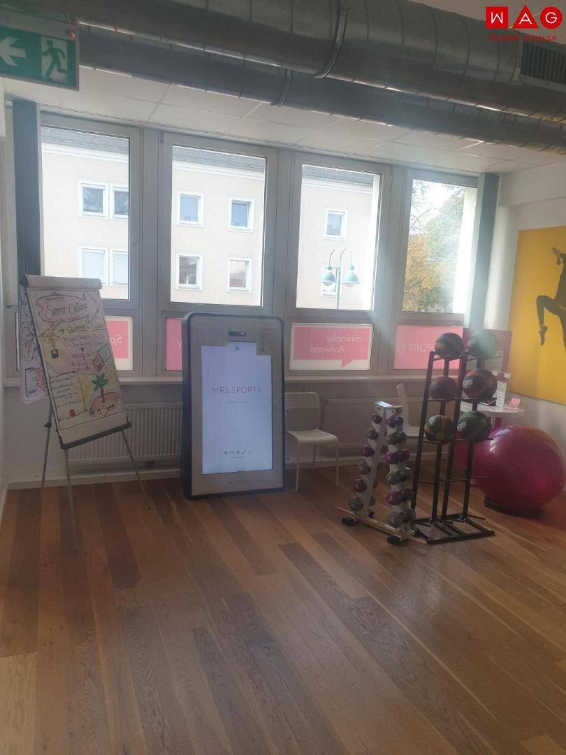 Trainingsraum mit Holzboden, großen Fenstern und einer Flipchart-Tafel.