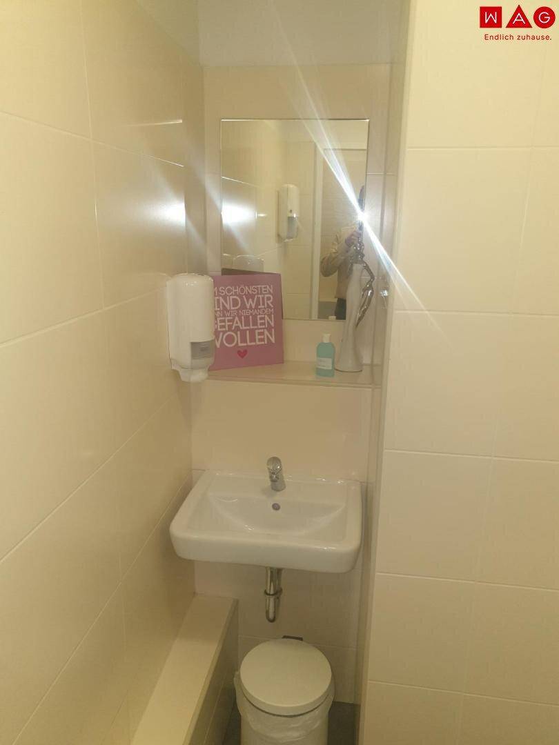 Kleines WC mit Waschbecken, Spiegel und Seifenspender, hell gefliest.