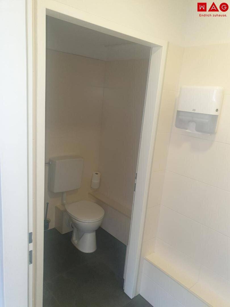 Einfaches WC mit Toilette und Papierhandtuchspender, hell gefliest.