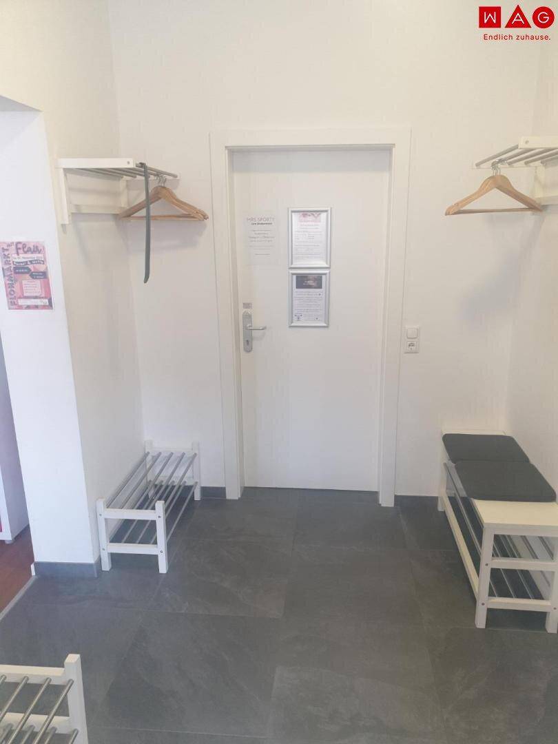 Eingangsbereich mit dunklem Fliesenboden, Garderobenständern und Schuhregalen.