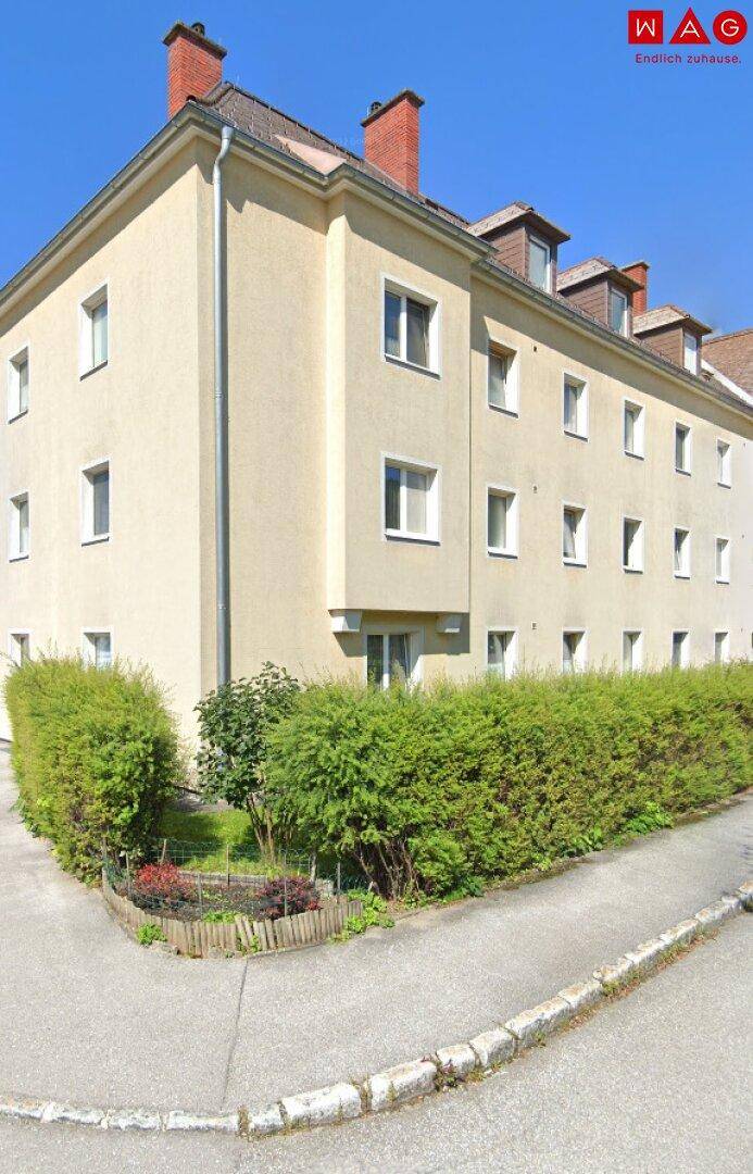 Mehrstöckiges Wohngebäude mit heller Fassade, vielen Fenstern und gepflegten Hecken im Vorgarten.