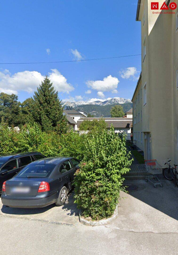 Außenansicht des Gebäudes mit Parkplätzen und einem beeindruckenden Bergblick im Hintergrund.