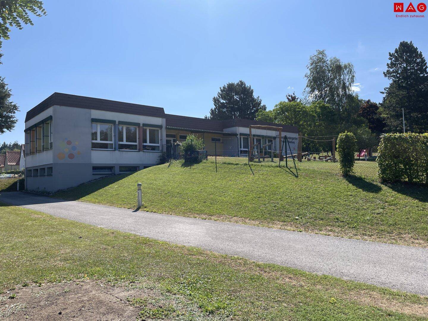 Modernes Gebäude mit Spielplatz und Grünflächen unter strahlend blauem Himmel.