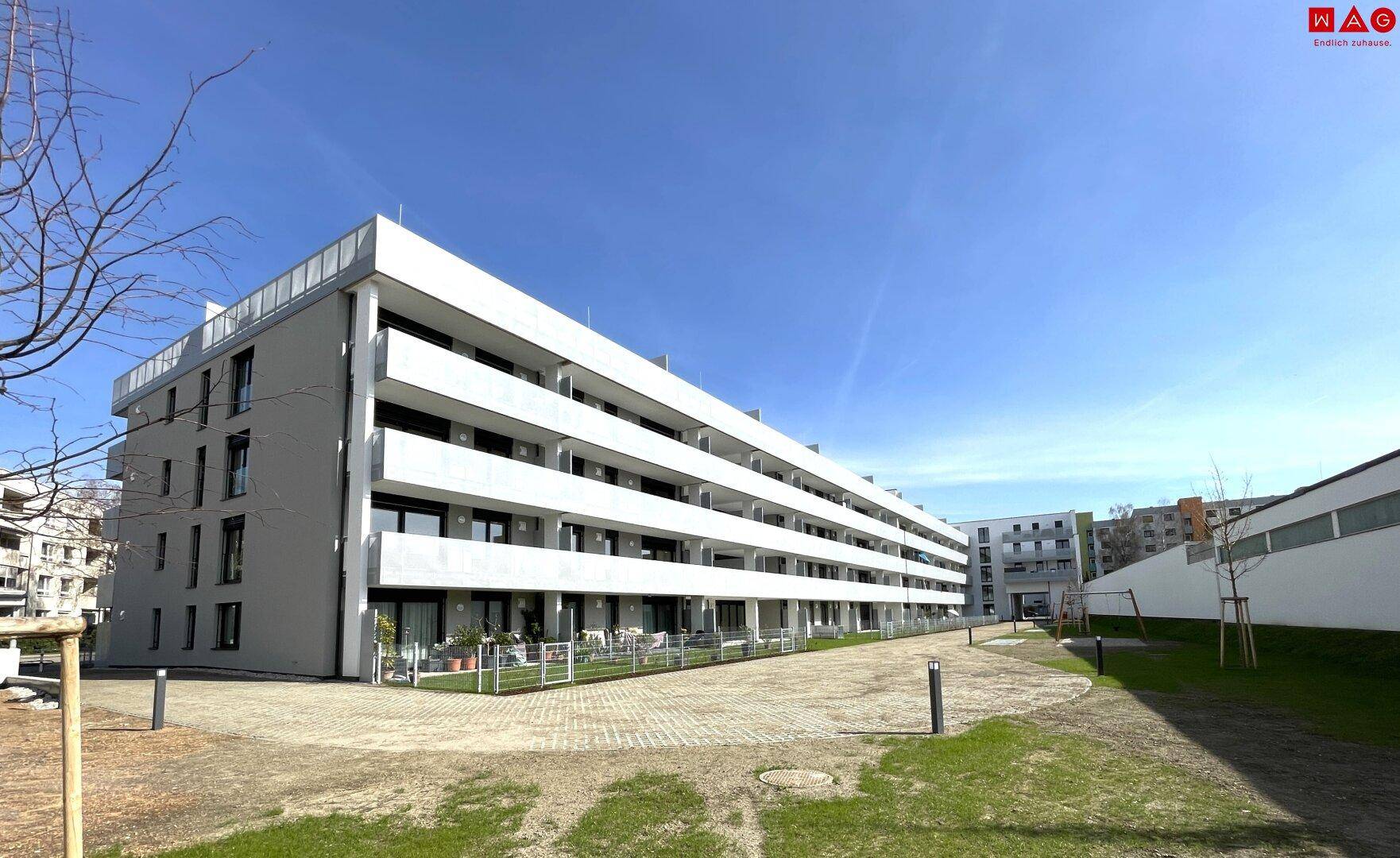 Außenansicht einer modernen Wohnanlage mit Grünflächen, Gehwegen und Spielplatz im Freien.