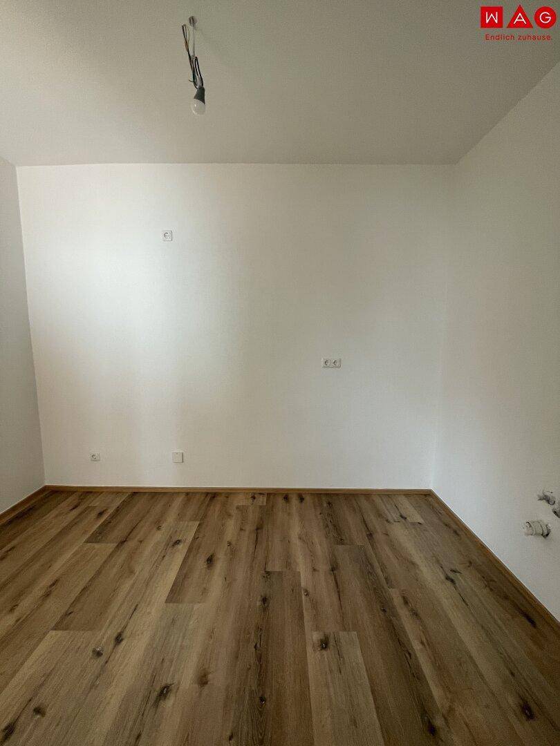 Leerer Raum mit hellem Laminatboden und weißen Wänden, vielseitig nutzbar.