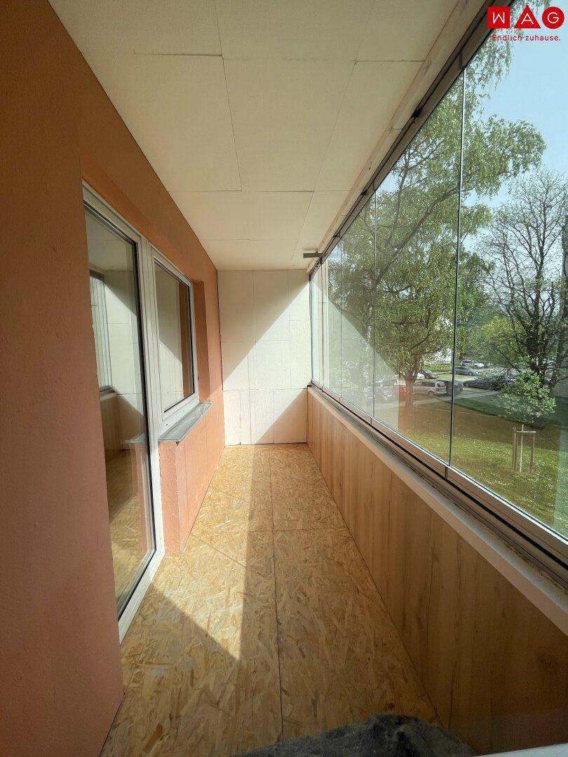 Langer, verglaster Balkon mit Holzboden und viel Tageslicht.