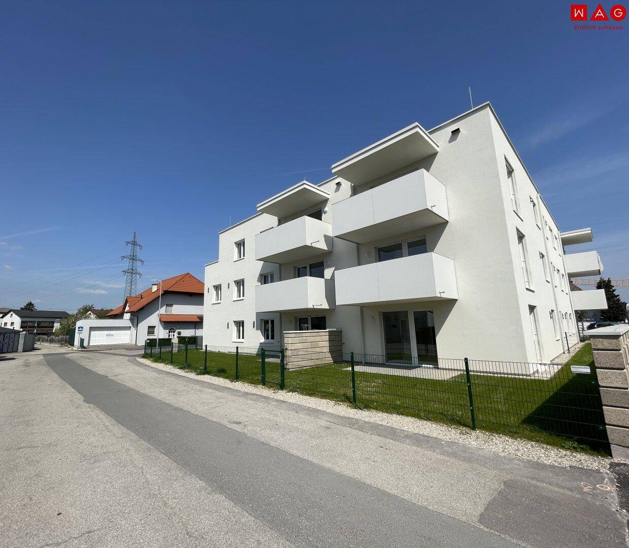 Modernes Mehrfamilienhaus mit weißen Fassaden, Balkonen und gepflegten Grünflächen in sonniger Lage.