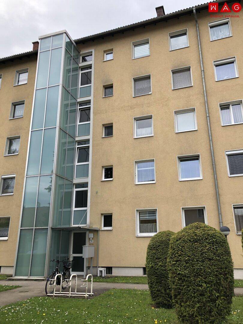 Mehrfamilienhaus mit moderner Glasliftanlage und gepflegter Fassade.