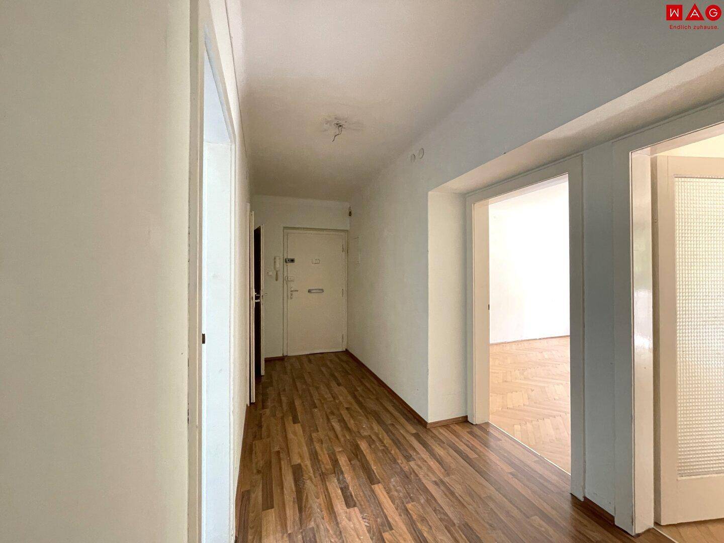 Langer Flur mit Holzlaminatboden und Zugang zu verschiedenen Räumen, inklusive der Eingangstür.