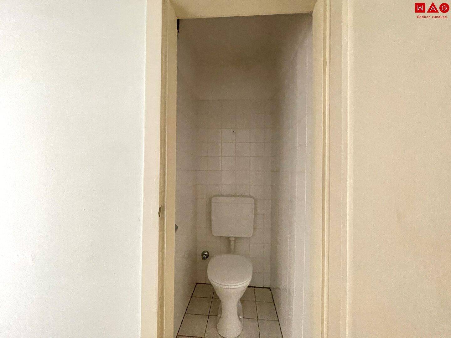 Separate Toilette mit Fliesenboden und Wänden, in einem kleinen, funktionalen Raum.