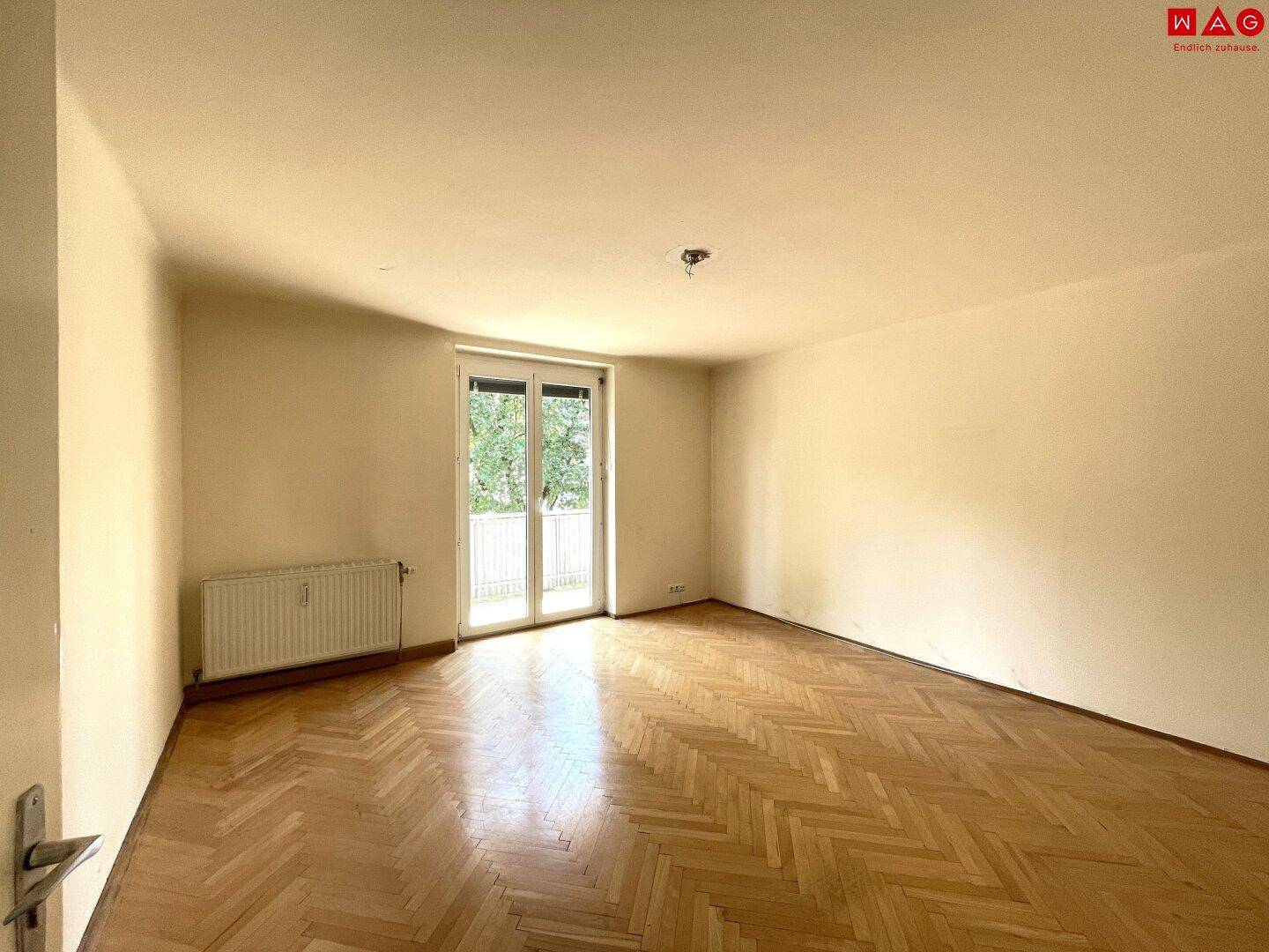 Helles Zimmer mit Fischgrätparkettboden und Zugang zu einem Balkon, ideal als Wohn- oder Schlafzimmer.