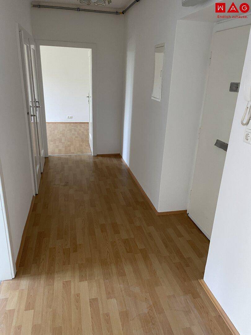 Heller Flur mit Holzboden, der zu weiteren Zimmern führt und eine Gegensprechanlage zeigt.