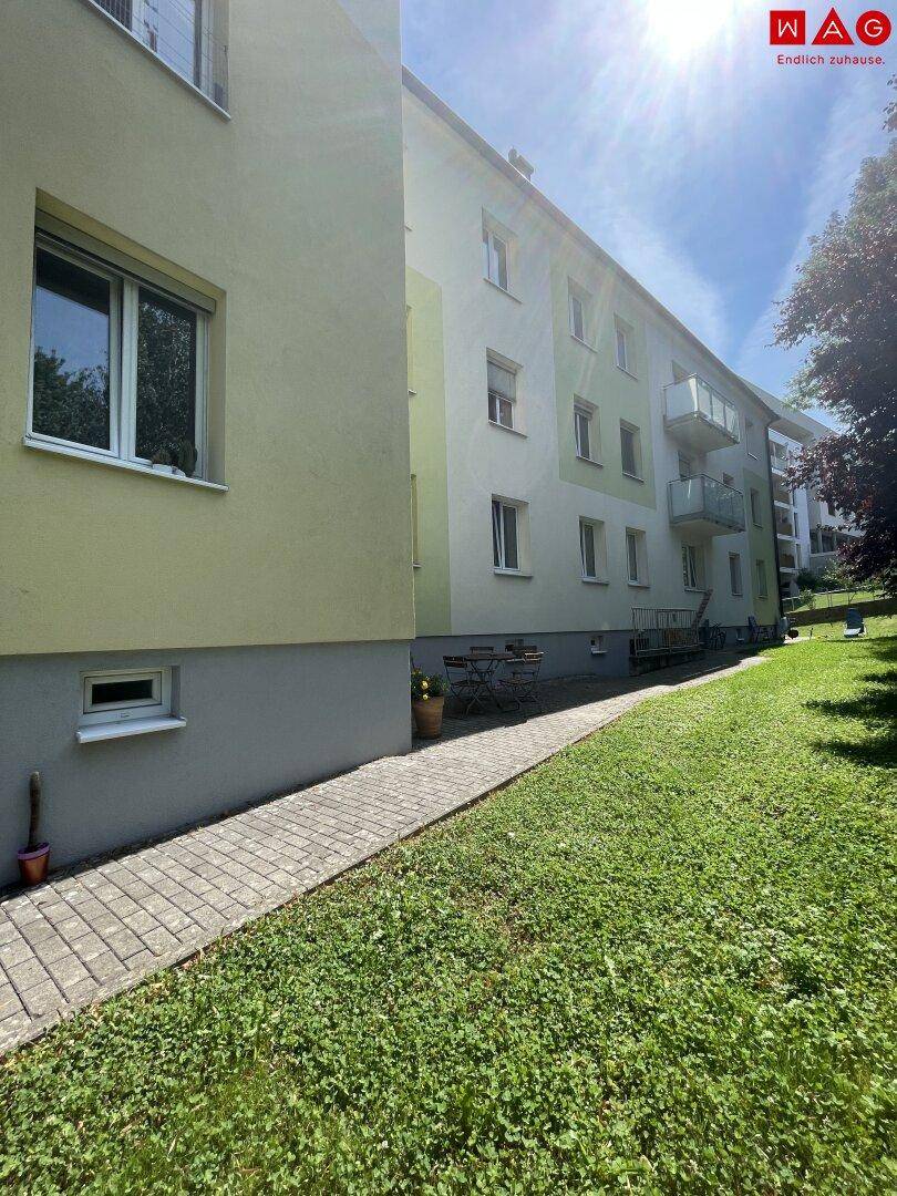 Mehrfamilienhaus mit gepflegter Fassade, Grünflächen und einem Gehweg im Außenbereich.