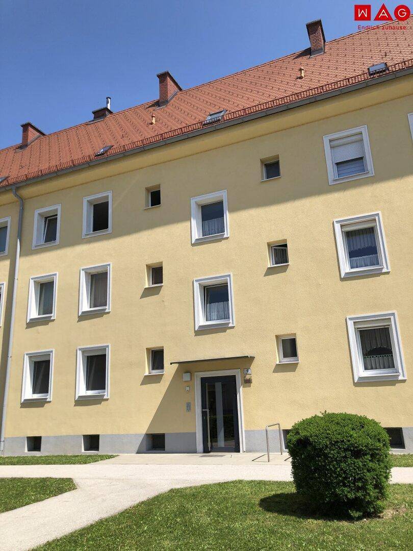 Gelbes Mehrfamilienhaus mit rotem Ziegeldach und gepflegter Fassade unter blauem Himmel.