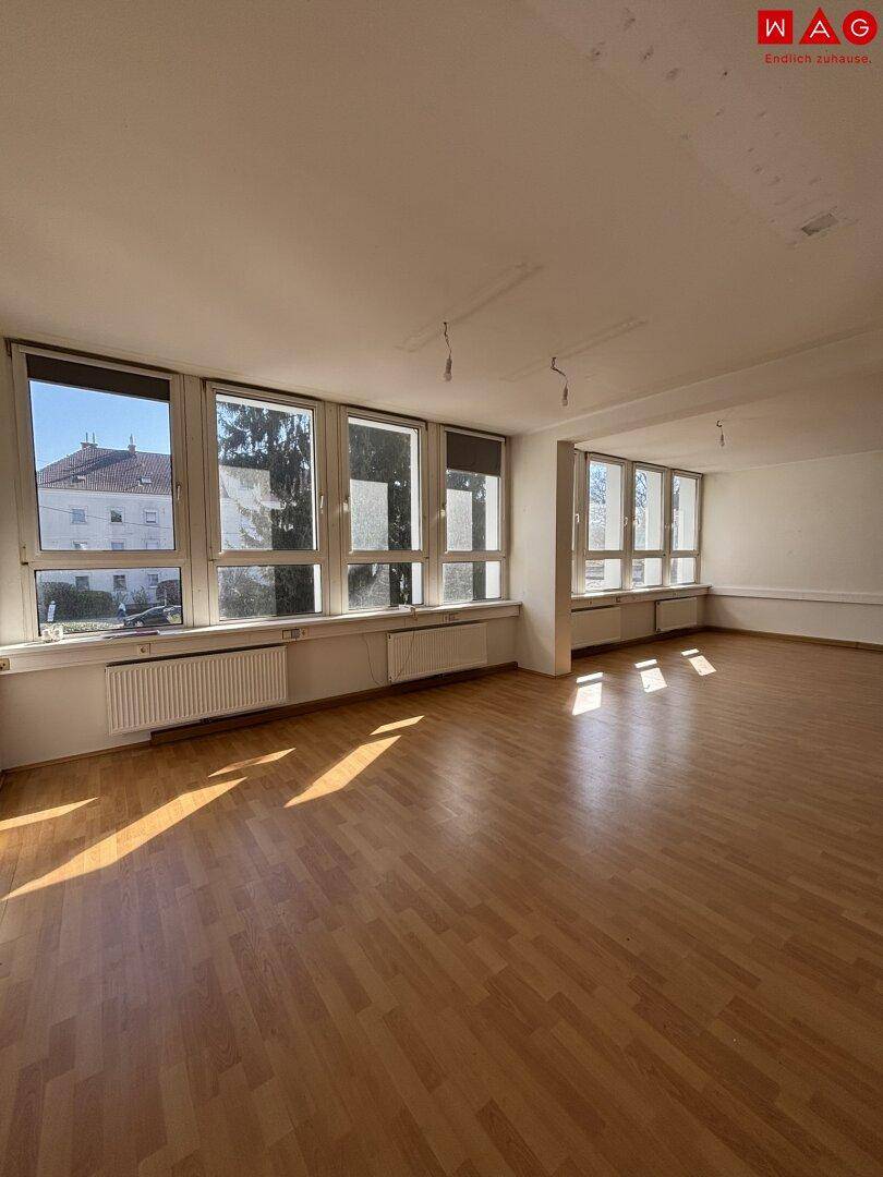 Großer, heller Raum mit Holzfußboden und vielen Fenstern, ideal für ein Büro oder Geschäft.
