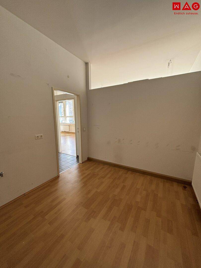 Kleinerer Raum mit Holzfußboden und einer Tür, die zu einem weiteren Bereich führt.