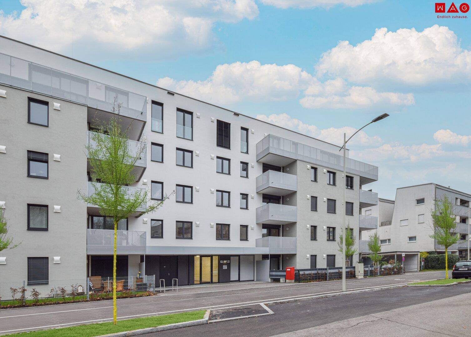 Moderne Wohnanlage mit mehreren Etagen, Balkonen und großen Fenstern in städtischer Umgebung.