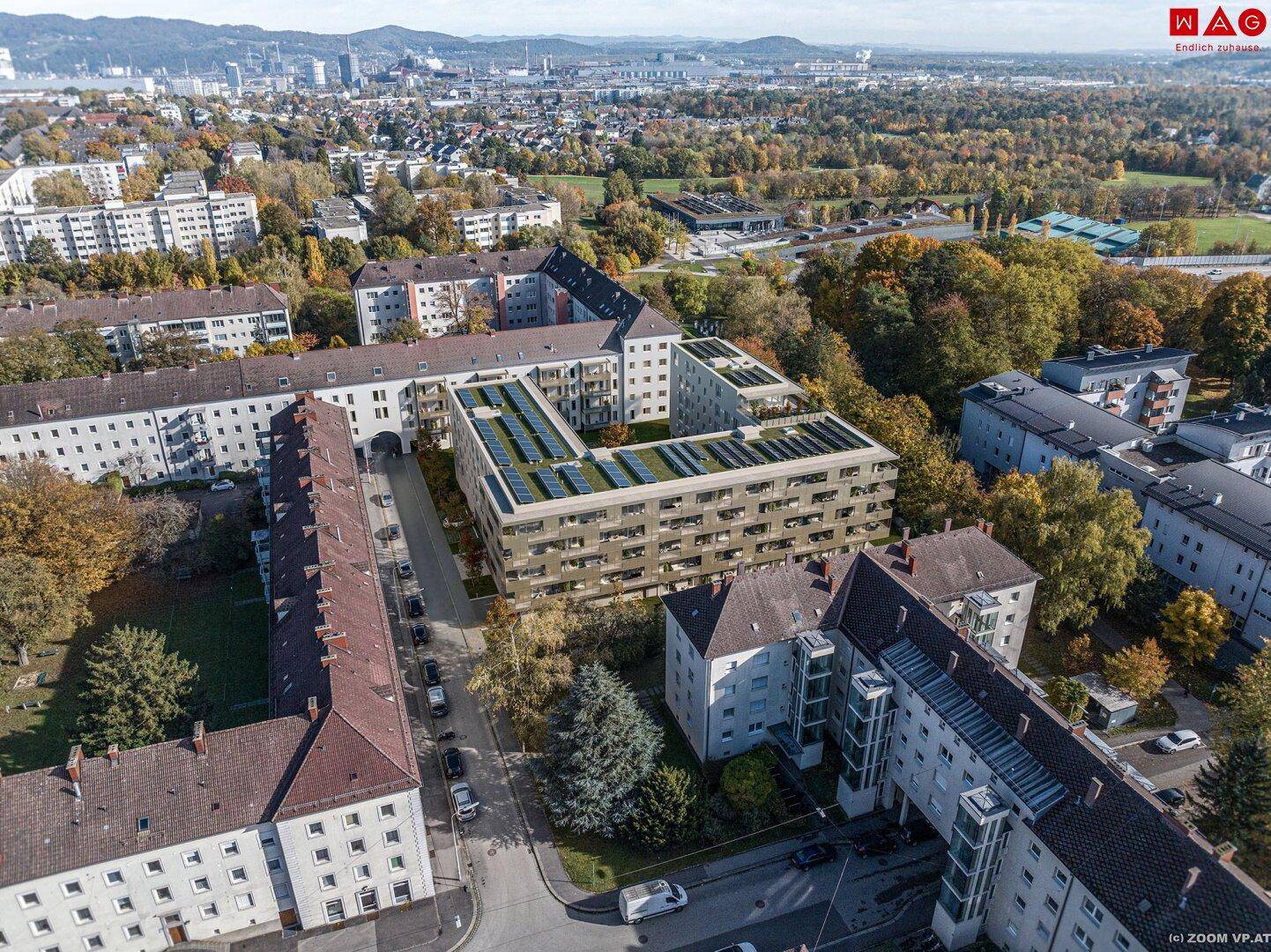 Luftaufnahme eines modernen Wohnkomplexes mit Gründächern und Solaranlagen in städtischer Umgebung.