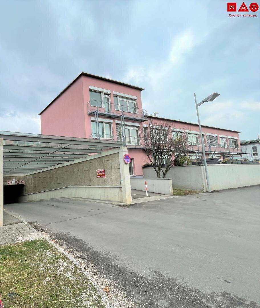 Außenansicht eines Wohngebäudes mit rosa Fassade und der Einfahrt zu einer Tiefgarage.