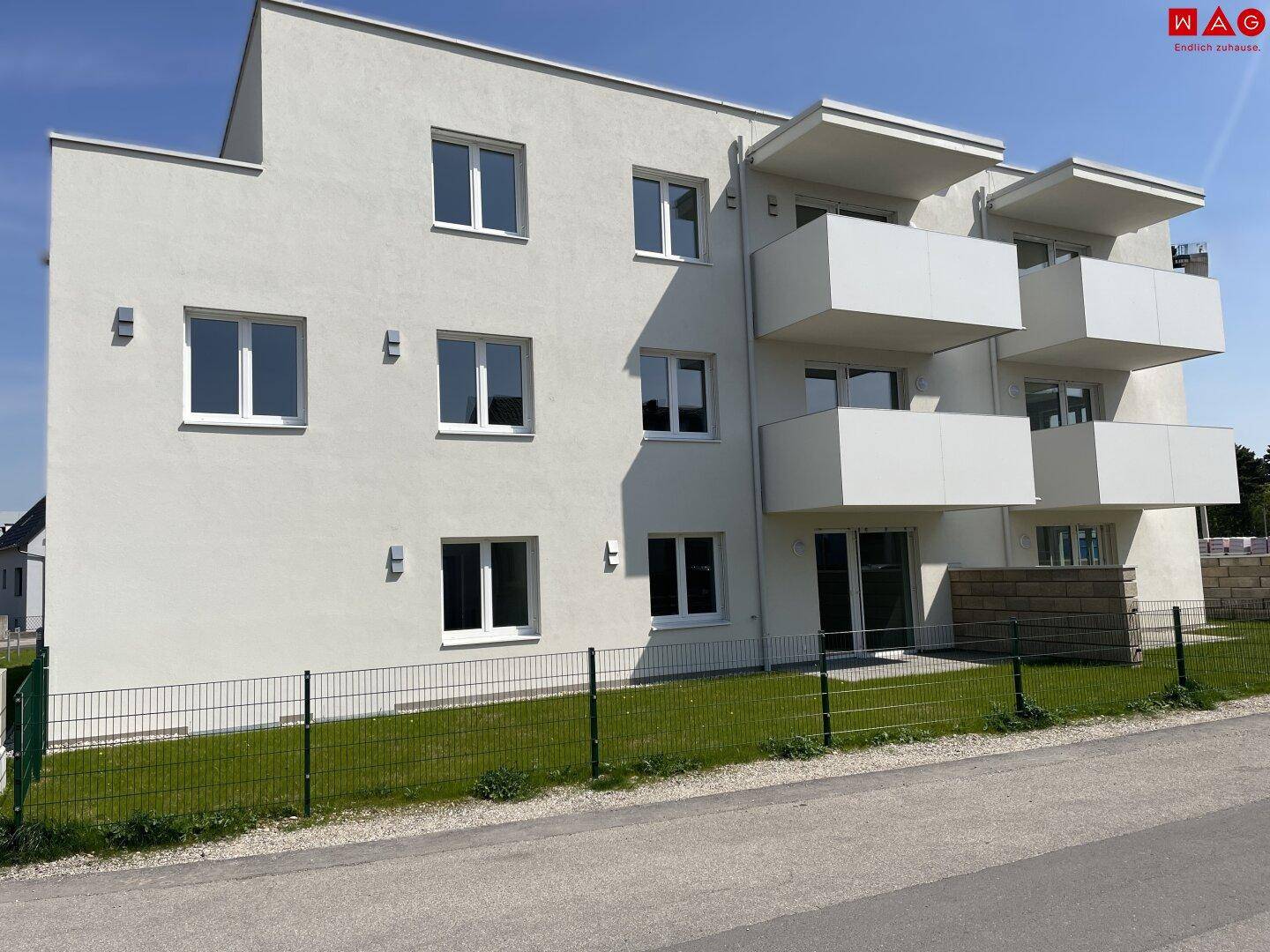 Seitenansicht des modernen Mehrfamilienhauses mit Balkonen und gepflegter Außenanlage.