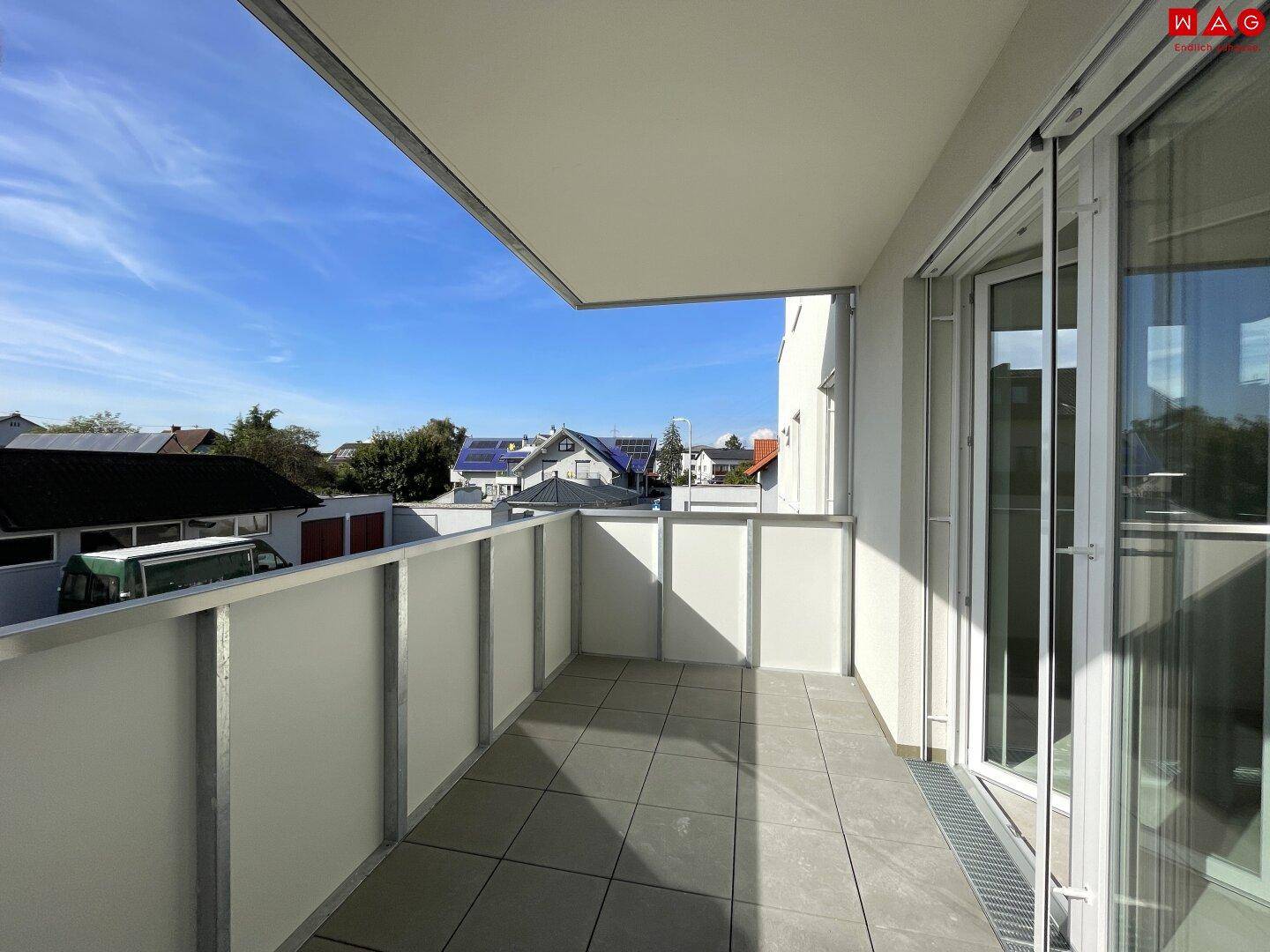 Geräumiger Balkon mit Fliesenboden und freiem Blick auf die Nachbarschaft unter strahlend blauem Himmel.