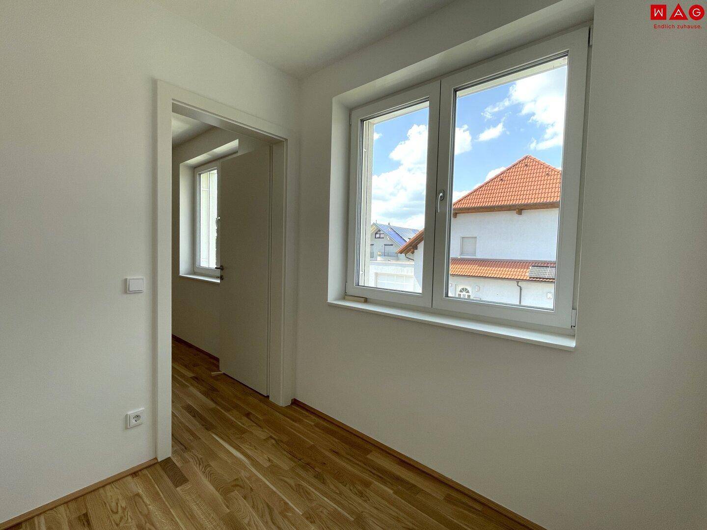 Heller Raum mit Holzboden und großen Fenstern, die einen Blick nach draußen bieten.