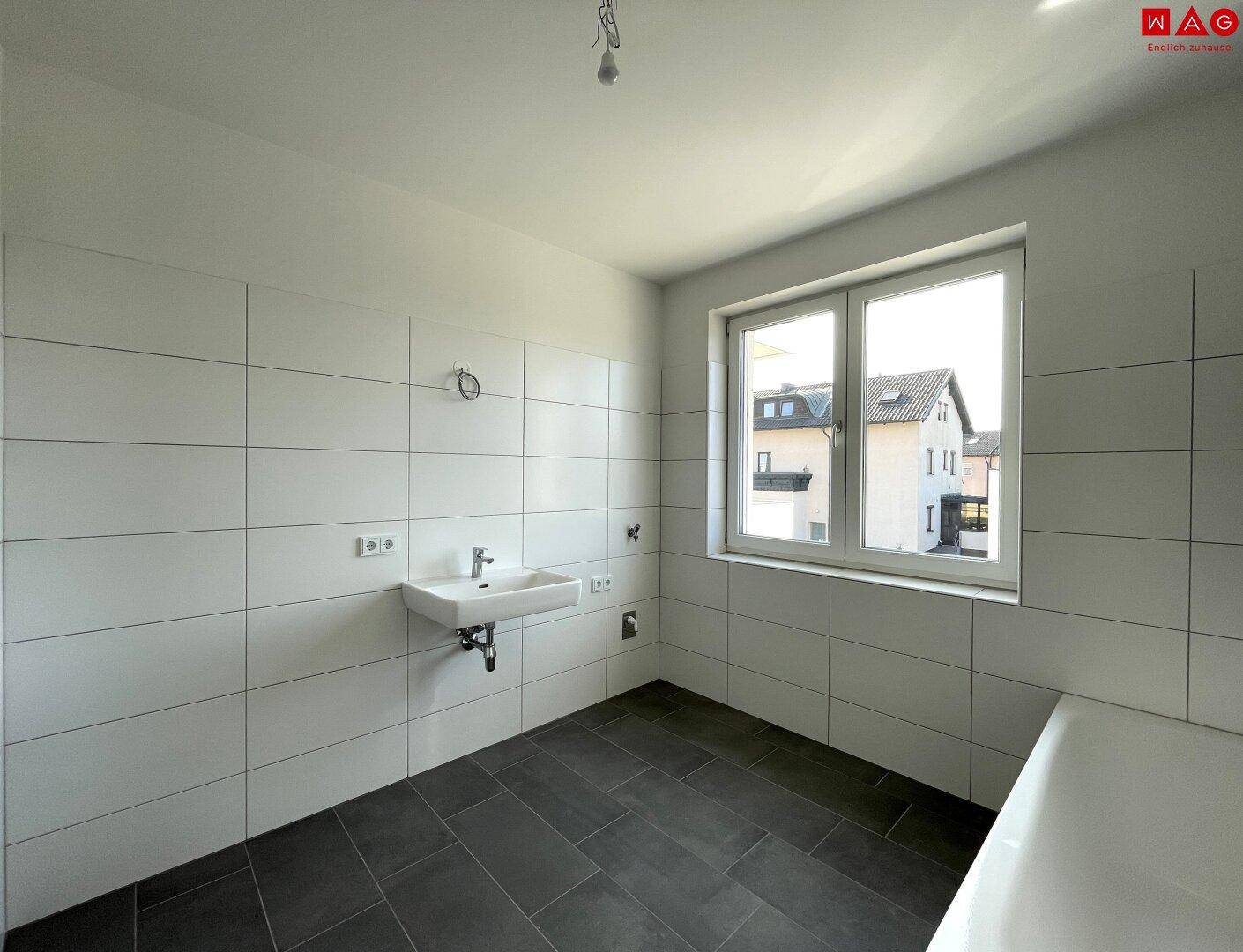 Helles Badezimmer mit weißen Fliesen, Waschtisch und Fenster für natürliche Belüftung.