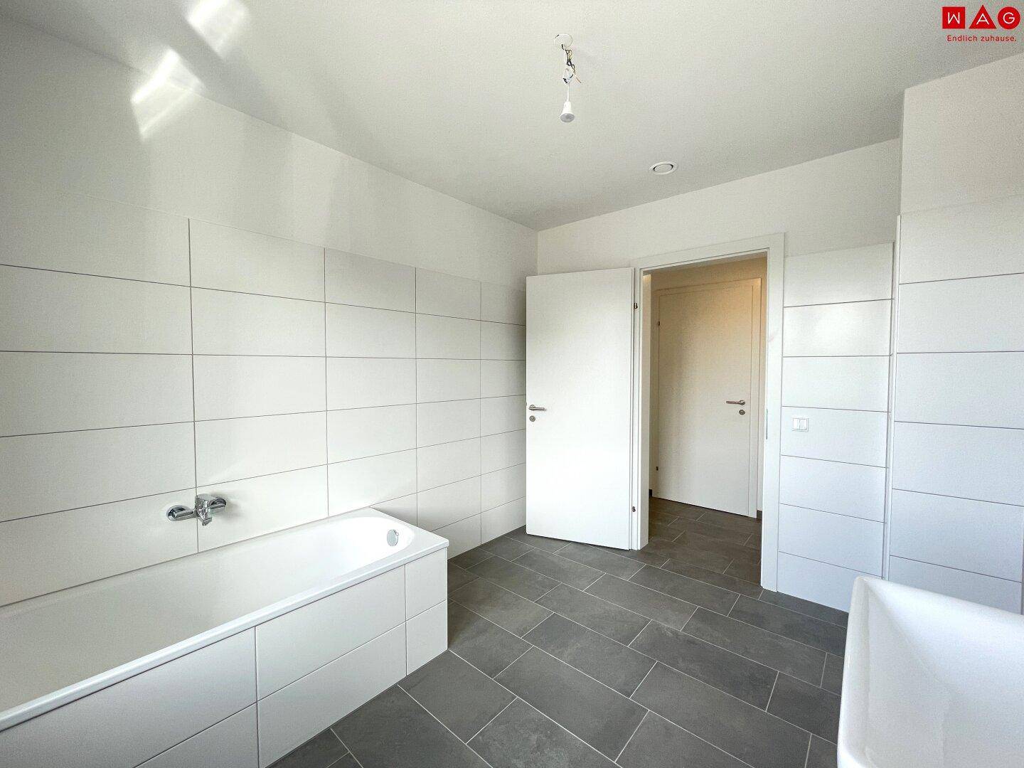 Helles Badezimmer mit Badewanne und Zugang zu weiteren Räumen, modern gefliest.