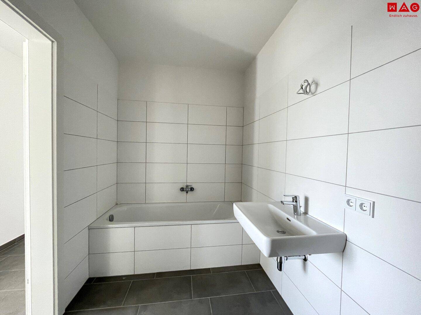 Helles Badezimmer mit Badewanne, Waschbecken und weißen Wandfliesen.