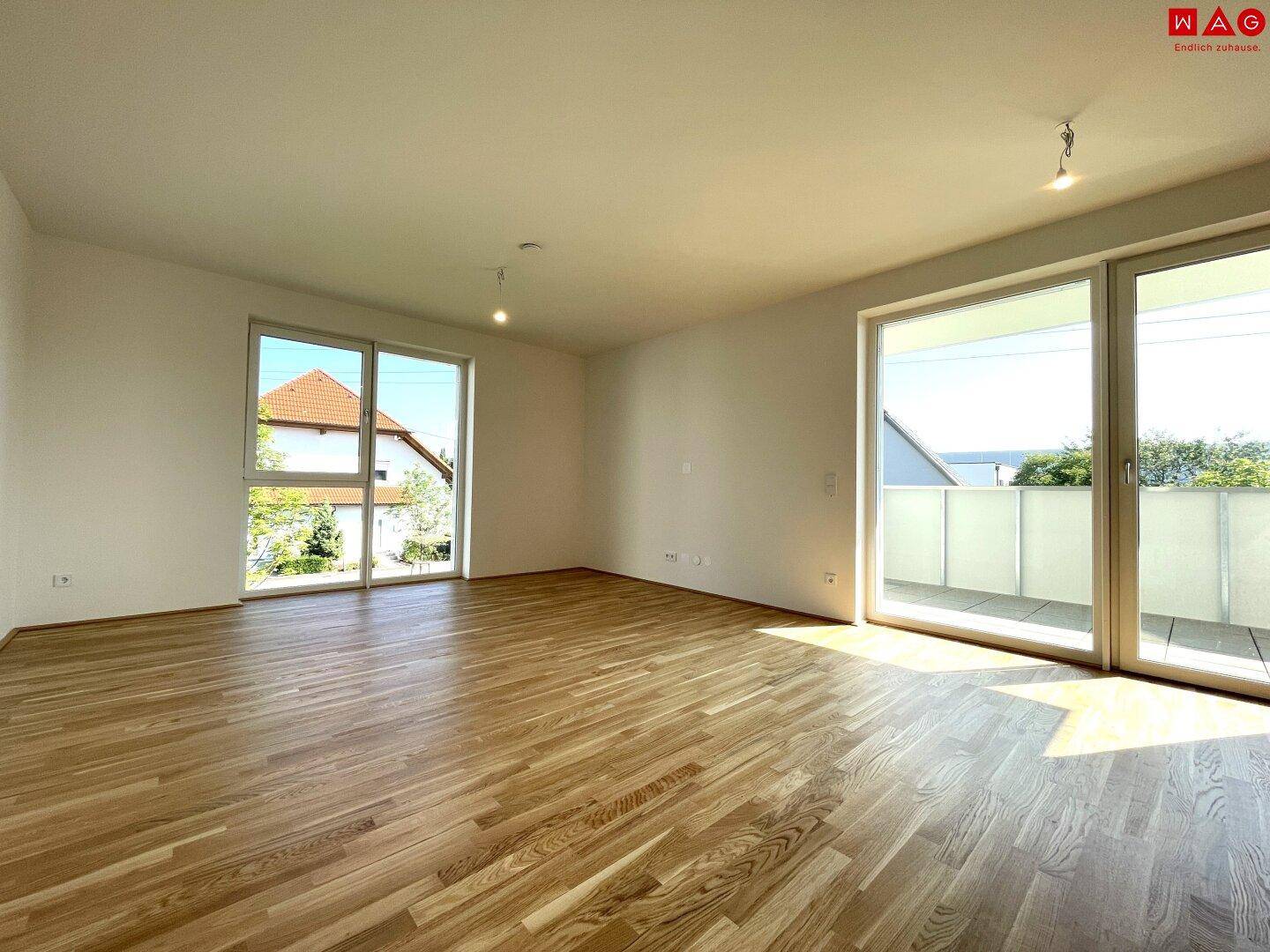 Helles Wohnzimmer mit Holzboden und großen Fenstern, die viel Tageslicht hereinlassen.