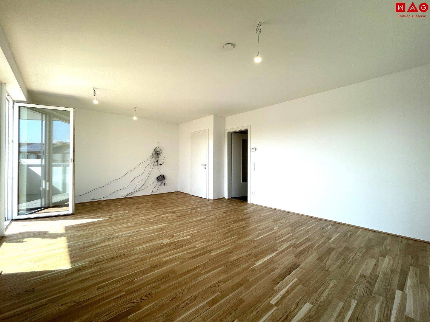Geräumiges Wohnzimmer mit Holzboden und Zugang zum Balkon, bereit zur individuellen Gestaltung.