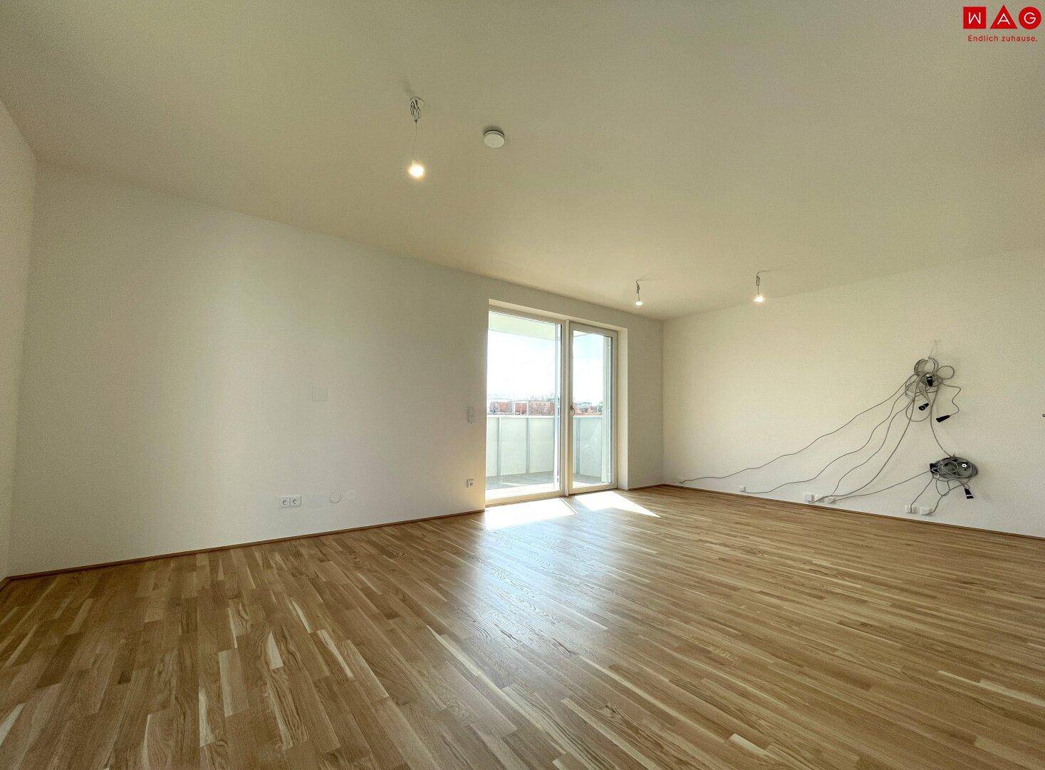 Geräumiges Wohnzimmer mit Holzboden und Zugang zu einem sonnigen Balkon.