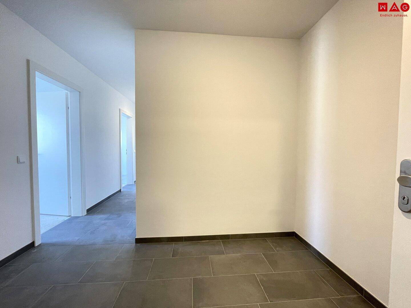 Heller Flur mit dunklem Fliesenboden, der zu verschiedenen Räumen führt und eine klare Raumaufteilung zeigt.