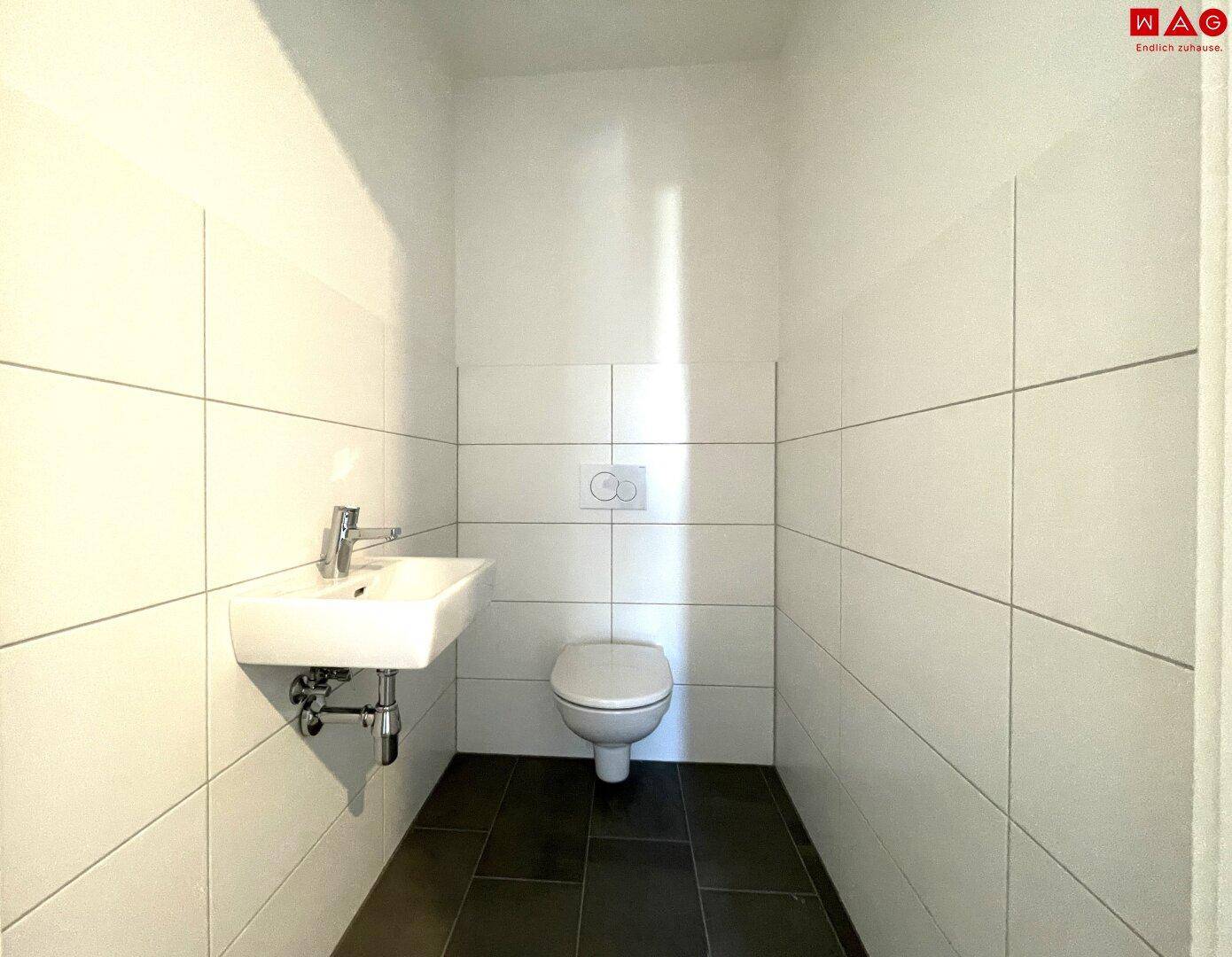 Helles Gäste-WC mit Fliesenboden und Wand-WC, bereit für die Endausstattung.