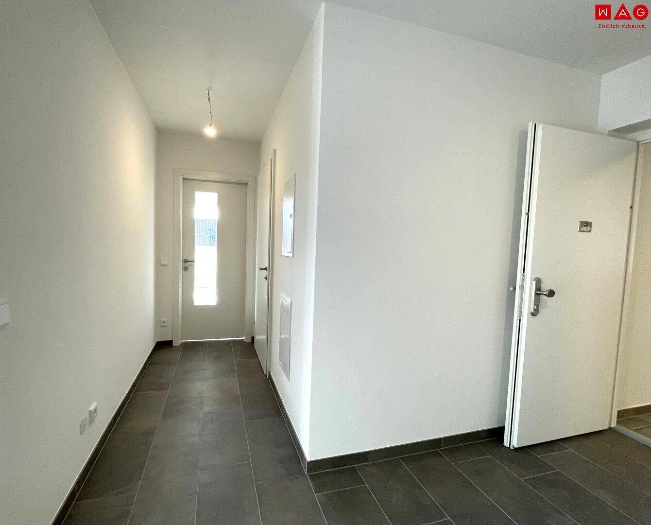 Leerer Flur mit Fliesenboden und weiß gestrichenen Wänden, schlicht und funktional.