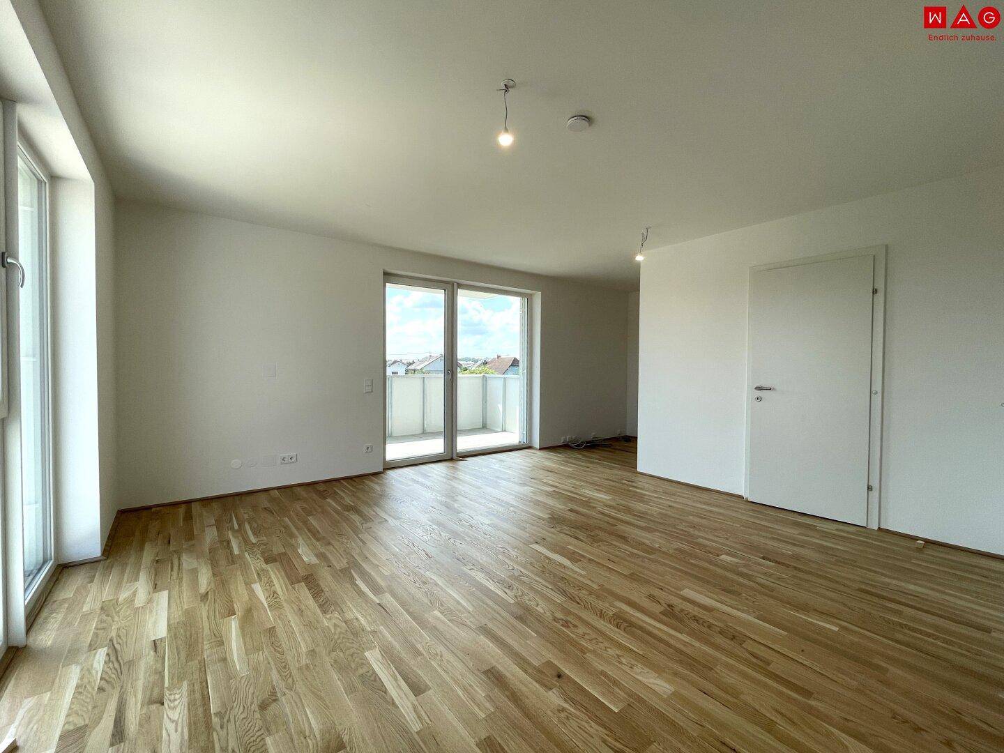 Geräumiger Raum mit Holzboden und großen Fenstern, ideal für Wohn- oder Essbereich.
