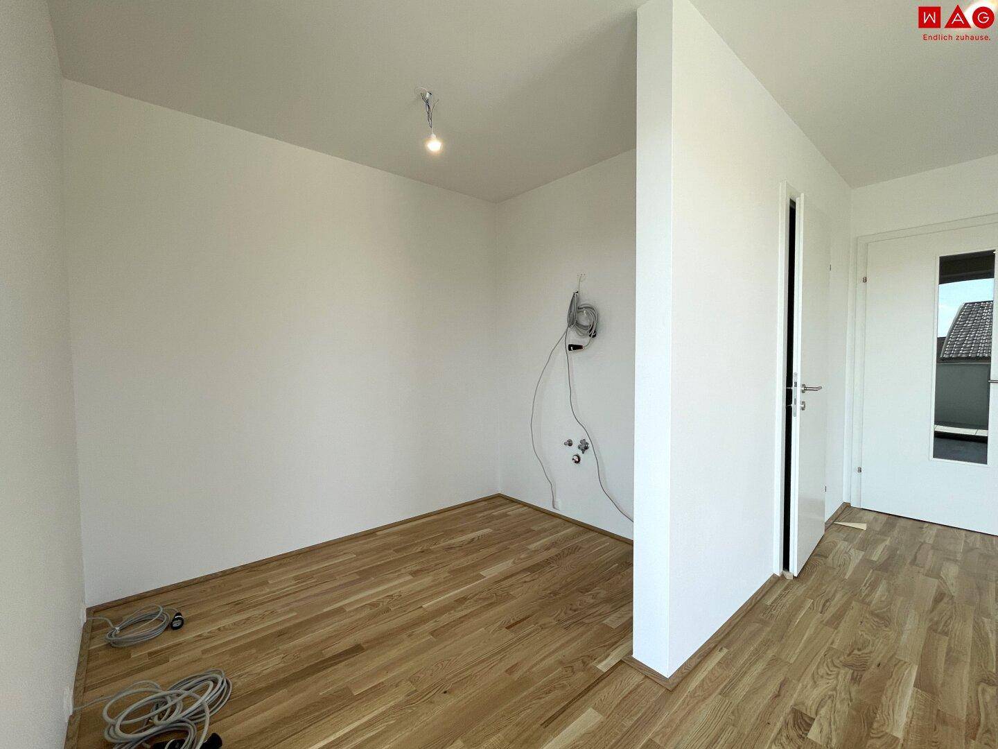Leerer Raum mit Holzboden und Anschlüssen für eine zukünftige Küche.