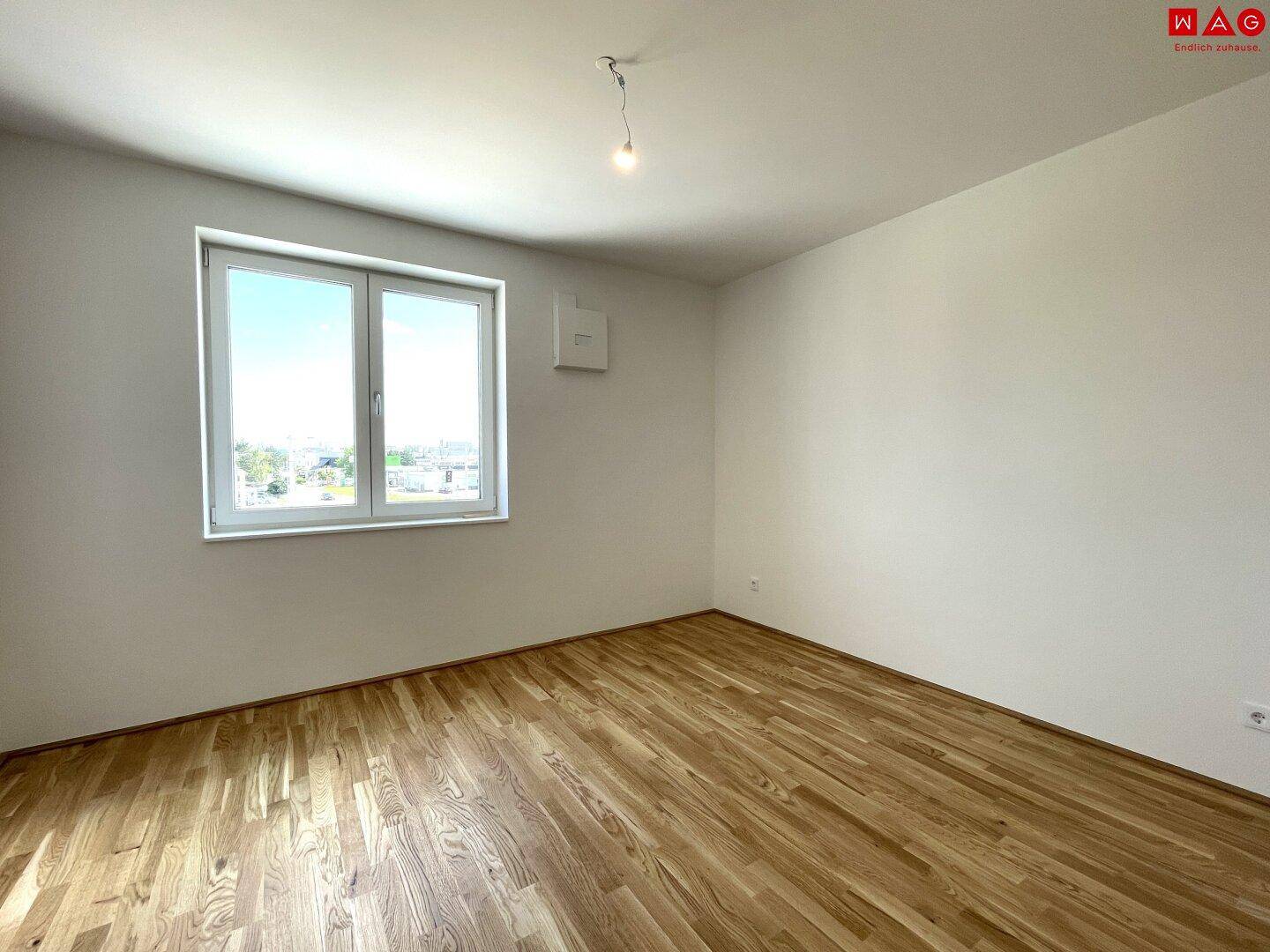 Helles Schlafzimmer mit Holzboden und großem Fenster, bereit zur individuellen Gestaltung.