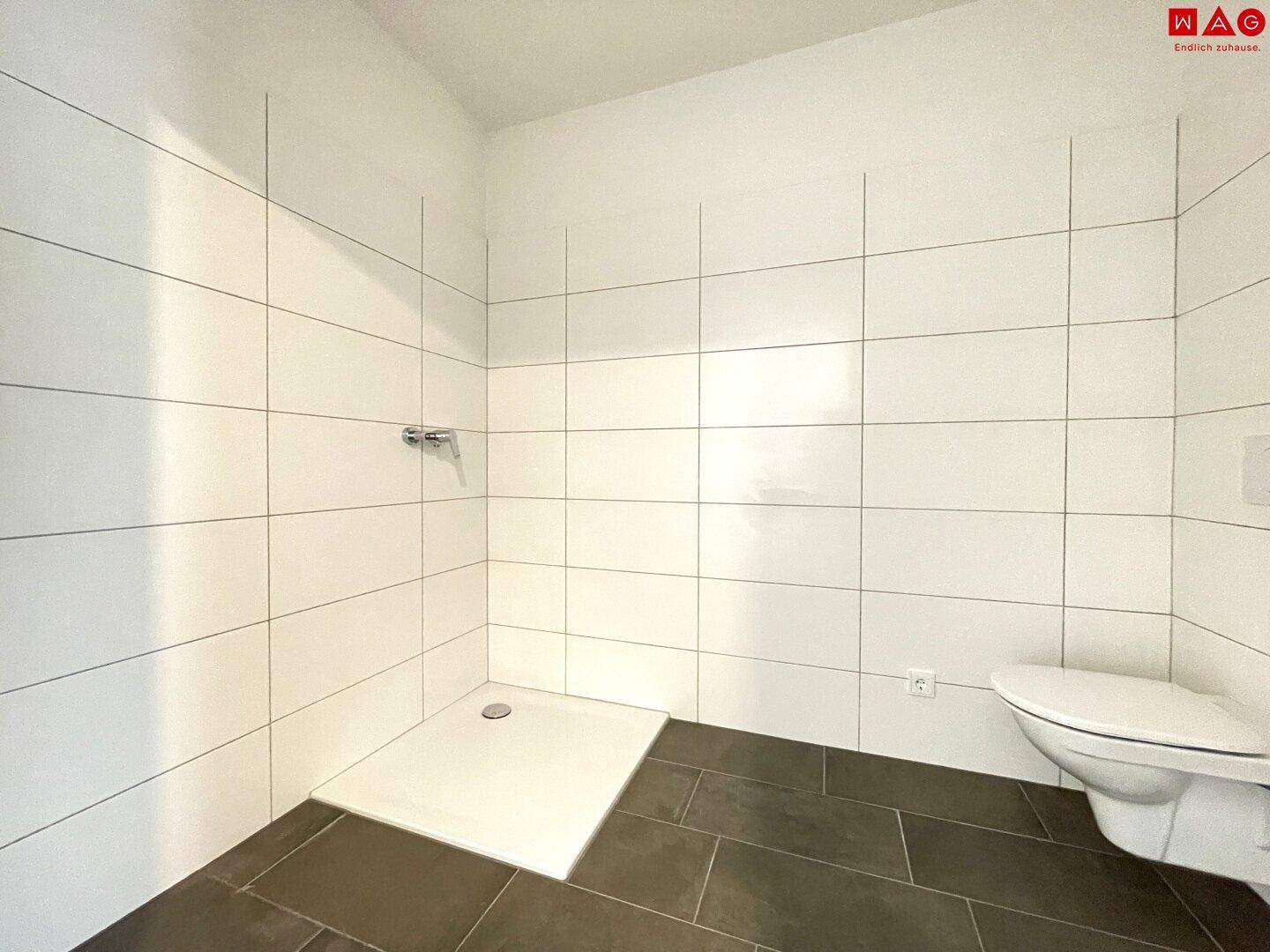 Leeres Badezimmer mit Duschbereich, WC und weißen Fliesen, bereit für die Installation der Armaturen.