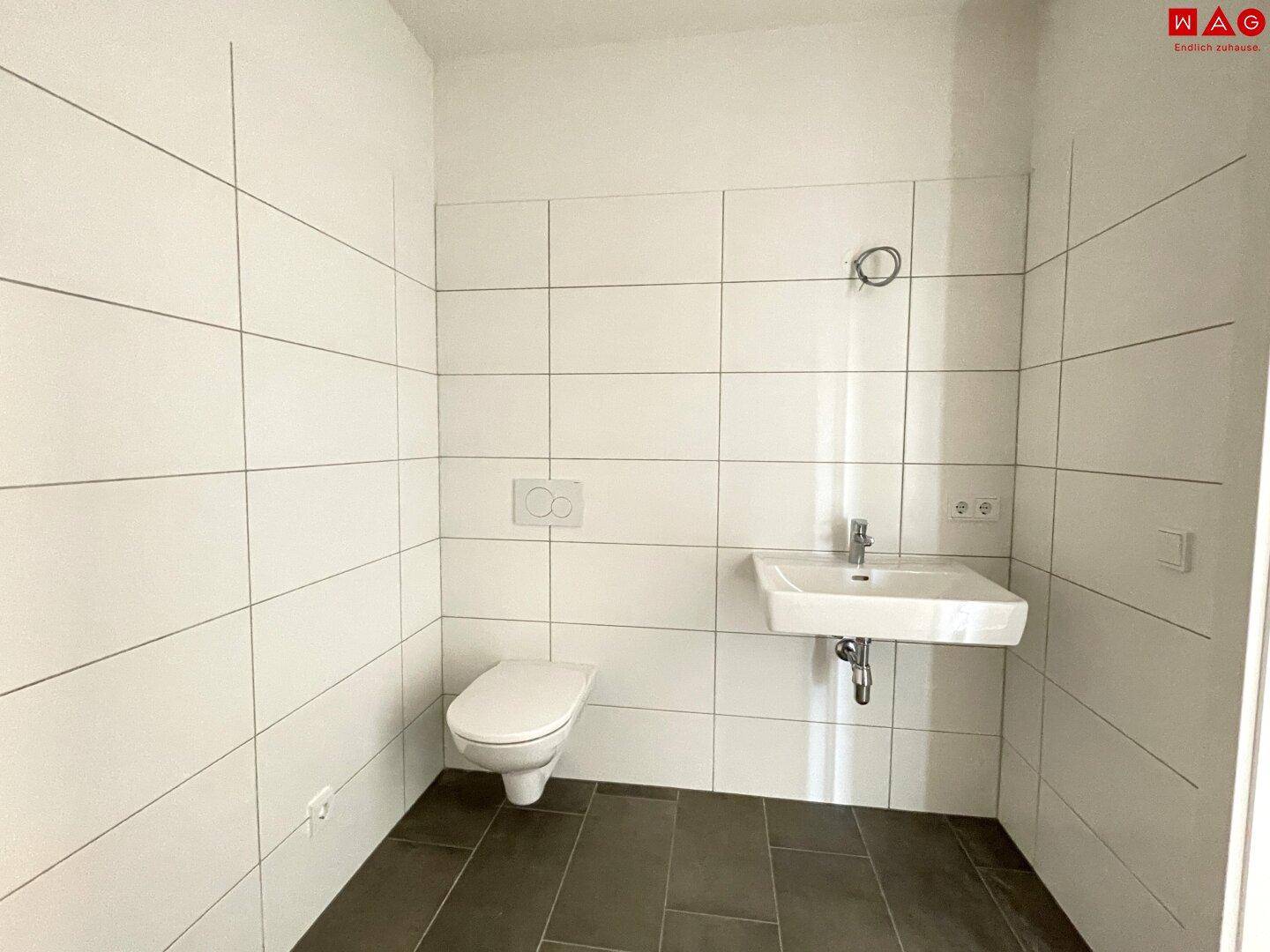 Helles Badezimmer mit WC, Waschbecken und weißen Wandfliesen, bereit zur individuellen Gestaltung.
