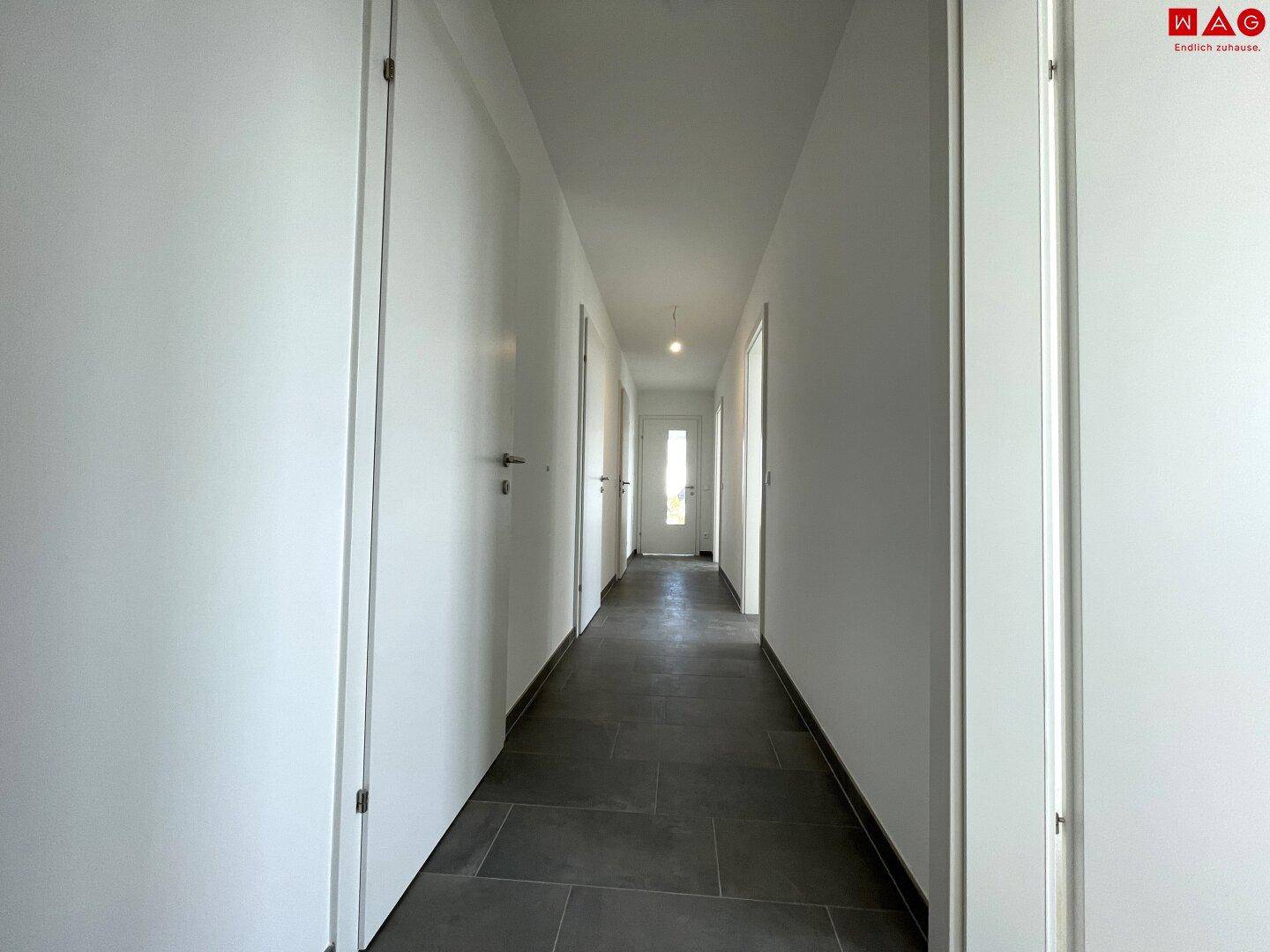 Heller Flur mit dunklen Fliesen und weißen Wänden, bietet einen klaren und aufgeräumten Durchgangsbereich.