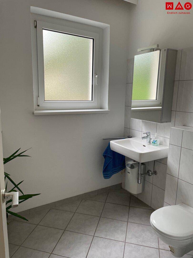 Modernes WC mit Fenster, Waschbecken und Wand-WC, ausgestattet mit hellen Fliesen.