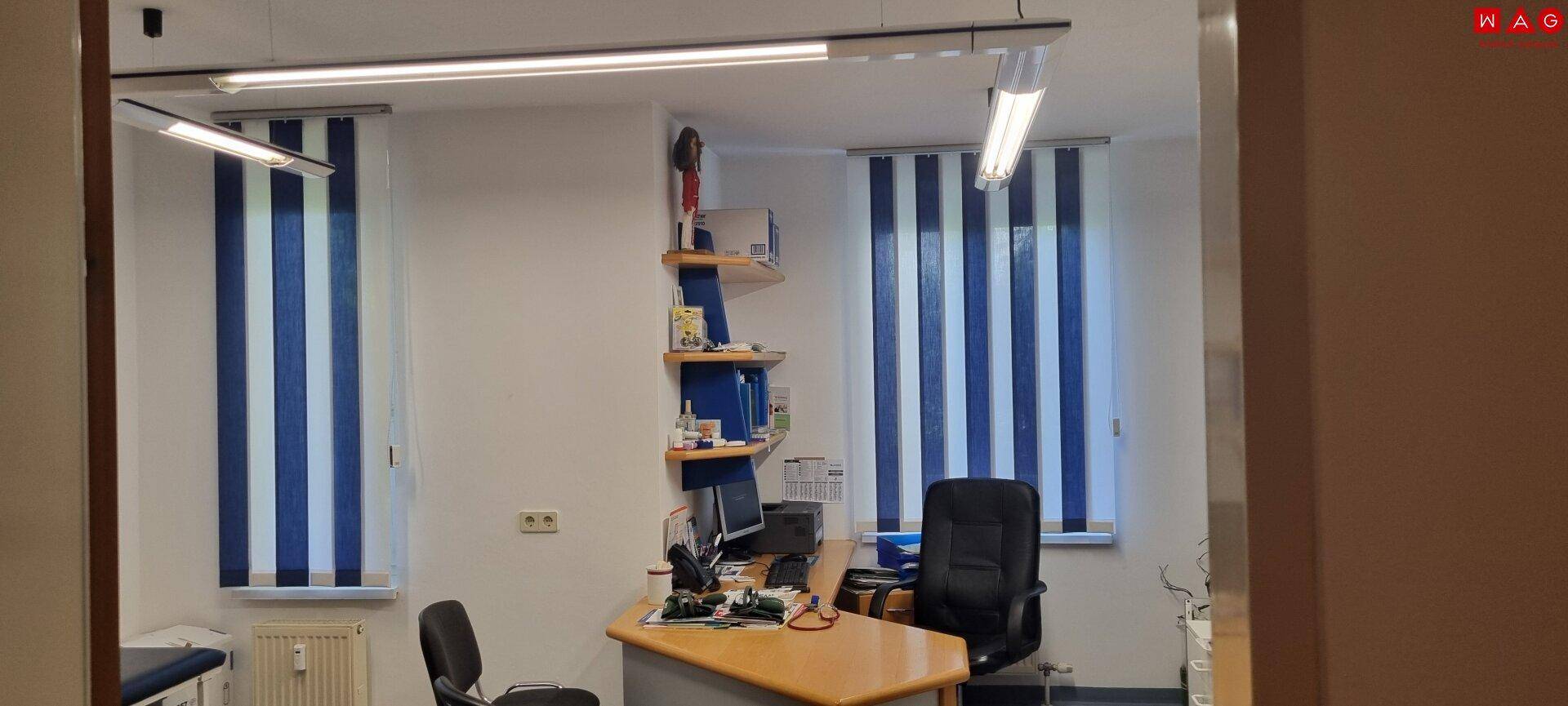 Funktionales Büro mit Schreibtisch, Bürostühlen und blau-weiß gestreiften Fensterrollos.