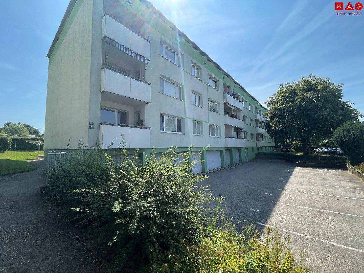 Gebäudefassade mit mehreren Balkonen und Garagen im Erdgeschoss unter blauem Himmel.