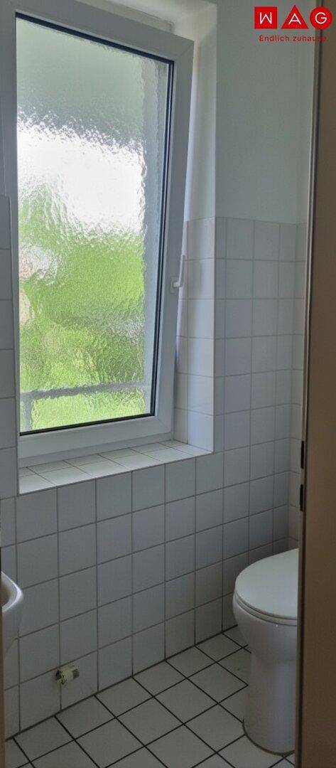 Kleines Badezimmer mit WC, Fliesenboden und einem Fenster mit Milchglas für Privatsphäre.