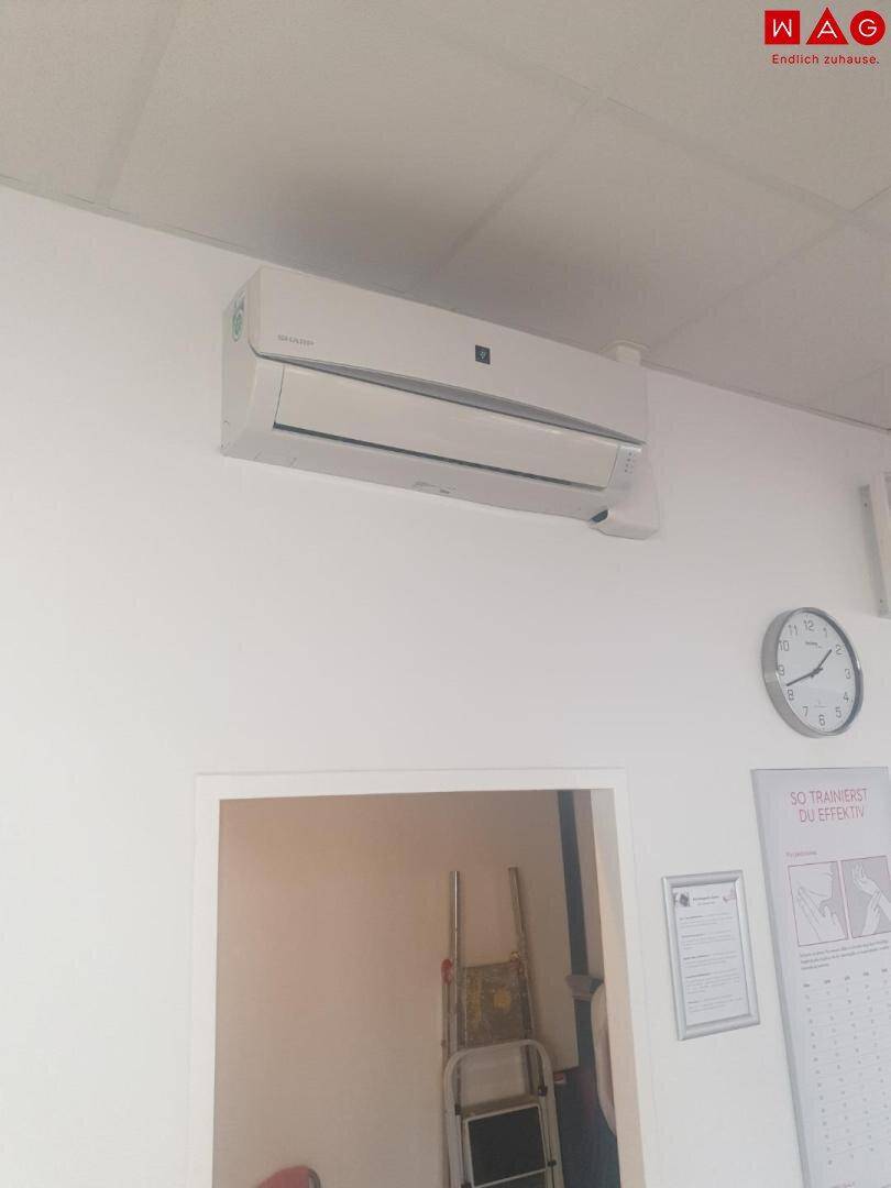 Klimaanlage an einer weißen Wand über einer Tür mit Uhr.