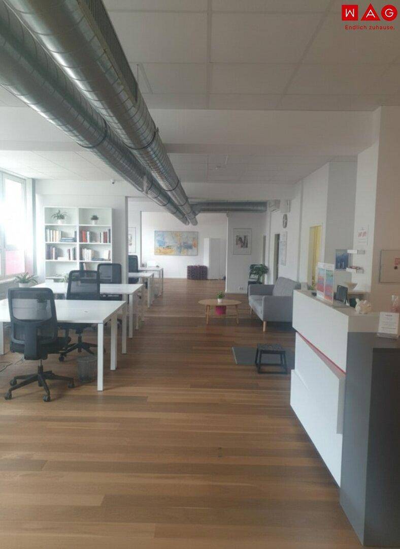 Offener Bürobereich mit Holzboden, mehreren Schreibtischen und einem Empfangsbereich.